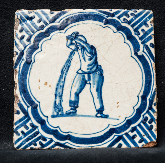 A rare early seventeenth century Delft blue tile with a vomiting man and Wanli corner decorations.