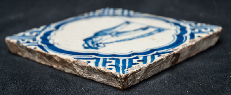 A rare early seventeenth century Delft blue tile with a vomiting man and Wanli corner decorations.