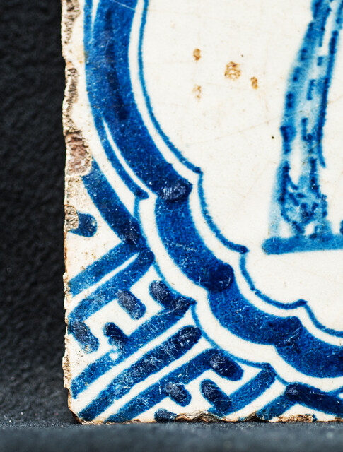 A rare early seventeenth century Delft blue tile with a vomiting man and Wanli corner decorations.