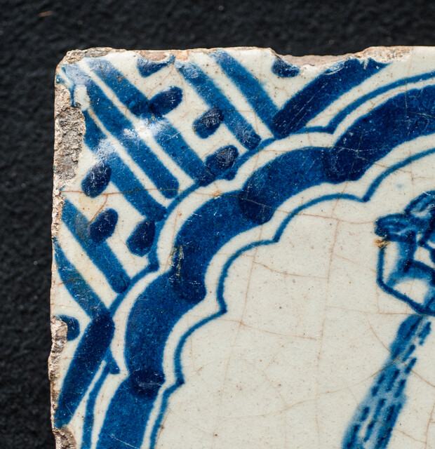 A rare early seventeenth century Delft blue tile with a vomiting man and Wanli corner decorations.