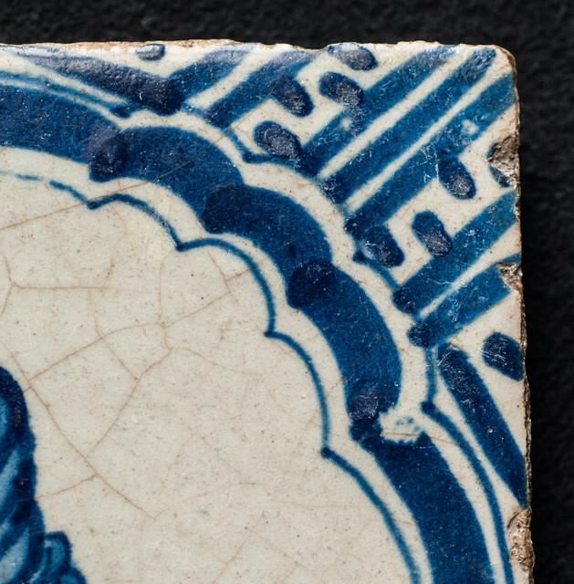 A rare early seventeenth century Delft blue tile with a vomiting man and Wanli corner decorations.