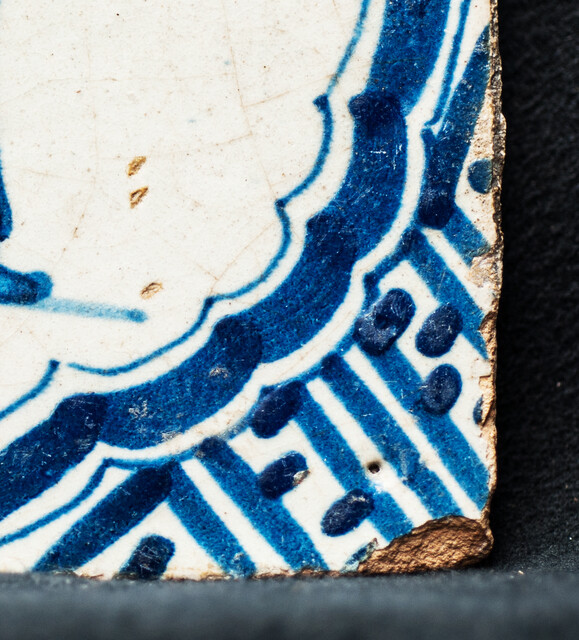 A rare early seventeenth century Delft blue tile with a vomiting man and Wanli corner decorations.