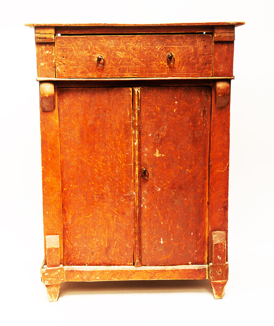 A red painted childrens cabinet with two doors and a drawer.