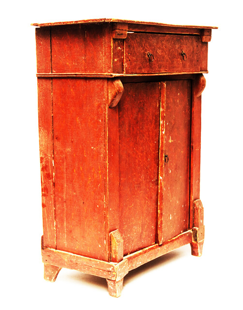 A red painted childrens cabinet with two doors and a drawer.