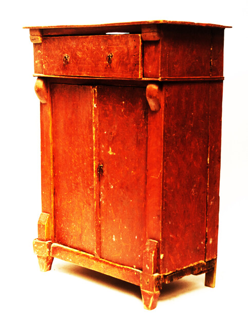 A red painted childrens cabinet with two doors and a drawer.