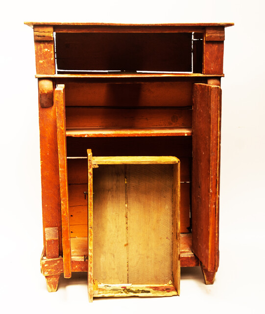 A red painted childrens cabinet with two doors and a drawer.