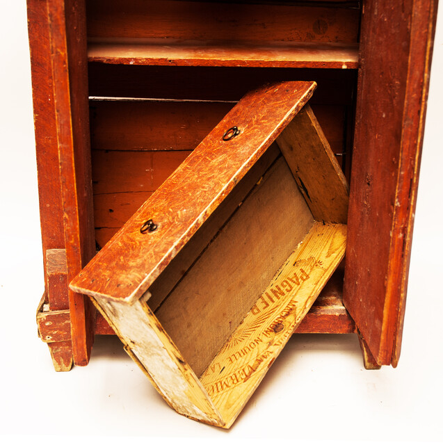 A red painted childrens cabinet with two doors and a drawer.