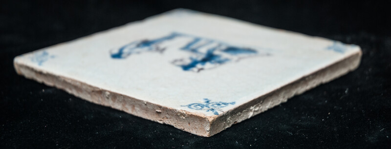 An early 17th C. Delft blue and manganese tile with two wool combers.